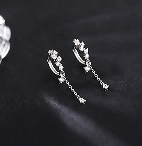 Elegant silver drop earrings with chain and crystal design on black background.