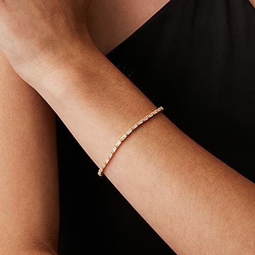 Person wearing a thin gold bracelet on their wrist.