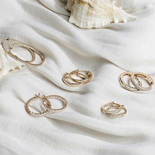 Gold hoop earrings displayed on white fabric with seashells.