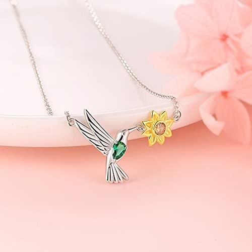 Silver hummingbird necklace with green gemstone and yellow flower pendant.