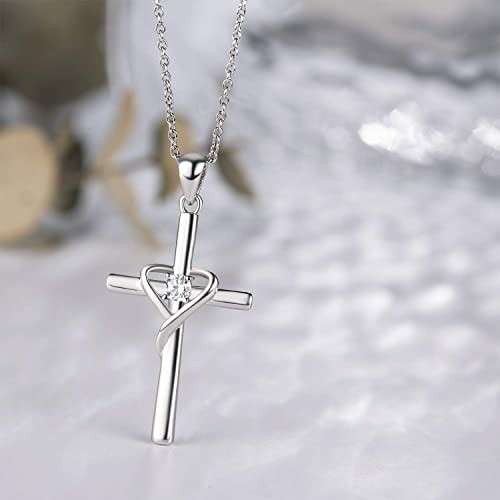 Silver cross pendant with heart design on a chain.