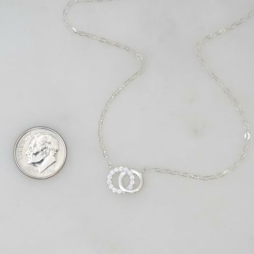 Silver necklace with a circular pendant next to a dime for size comparison.