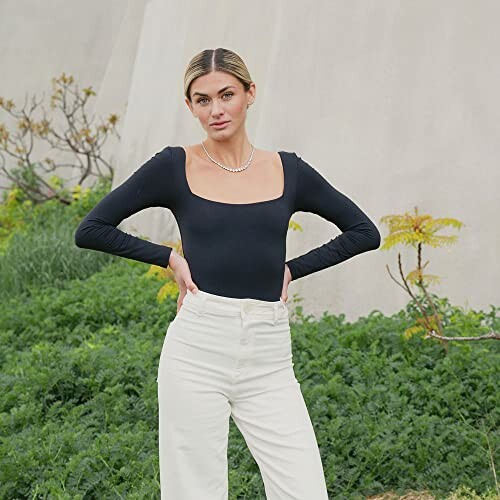 Woman wearing a black square-neck top and white pants standing outdoors